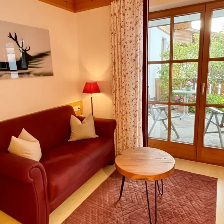 Gemütliche Wohnzimmer mit Sofa, Beistelltisch und Blick auf die Terrasse in der Ferienwohnung Alpenrose im Haus am Wiesbach, reit im Winkl